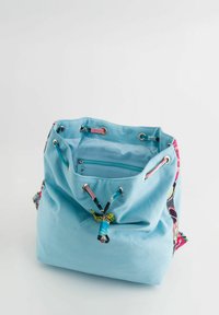 Bolso cubo de tela azul claro con acentos de patrones coloridos, cierre de cuerda y bolsillo interior con cremallera. Textura suave y diseño espacioso.