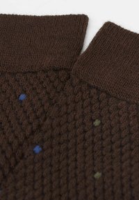Tessuto marrone con un design a maglia testurizzato. Presenta puntini multicolore in blu e verde. Visibili due bordi distinti del colletto.