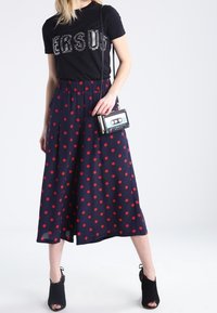 Camiseta negra con texto brillante, falda marinera con lunares rojos, y un pequeño bolso negro en forma de cinta de casete. Zapatos negros de punta abierta.