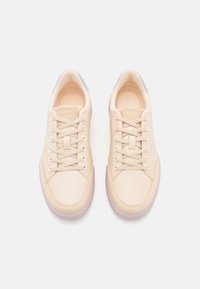 Zapatillas de cuero beige con una textura suave; puntera redondeada, cordones blancos y acentos lavanda en el talón y la lengua. Suela de goma.