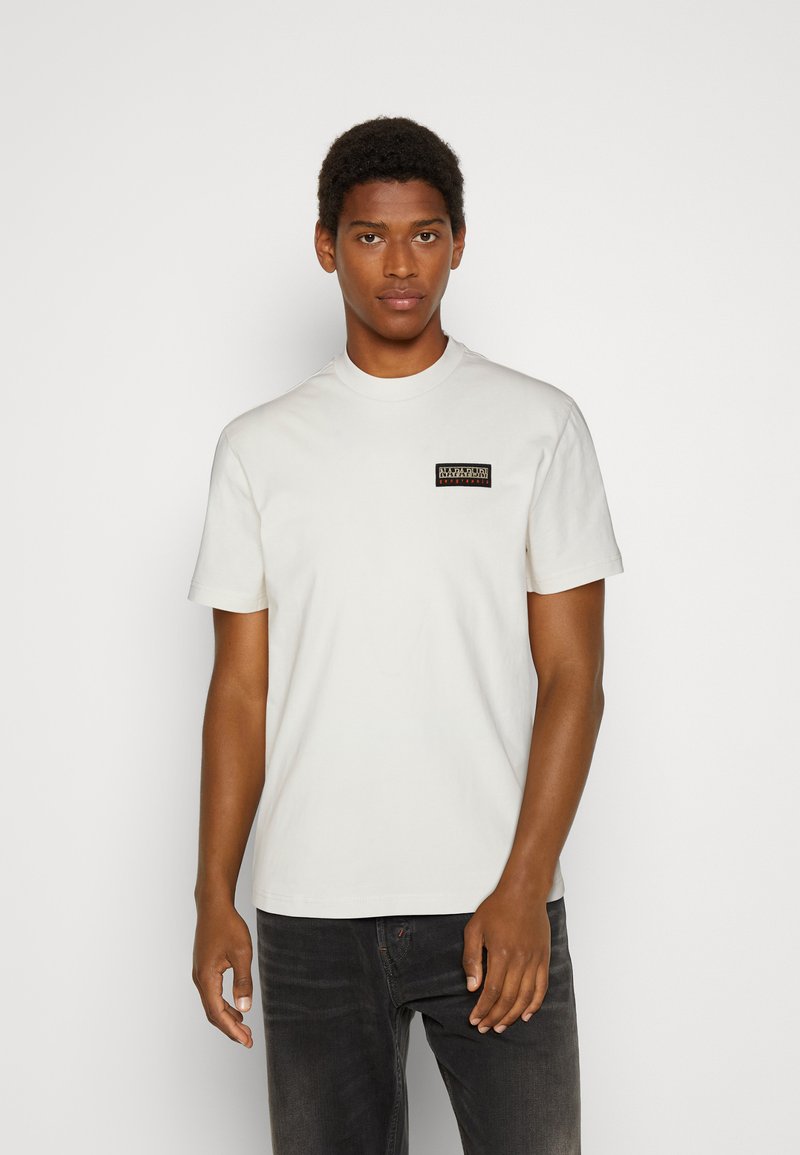White cotton t-shirt with a crew neckline and short sleeves, featuring a small rectangular black and multicolored logo at the chest.