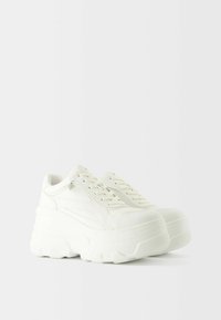 Sneakers platform bianchi con parte superiore in pelle liscia, suola spessa e texture, e punta rotonda. Presenti lacci e dettaglio con zip laterale.