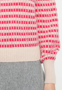 Sweter dzianinowy w różowo-białą kratkę, z prążkowanymi mankietami i dołem w odcieniu beżu. Miękka tekstura, lekko puffowane rękawy i dopasowany fason.