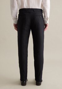 Pantalones de lino negros con un diseño de pierna recta, que cuentan con dos bolsillos traseros con botones y una textura suave, usados con una camisa de color claro.