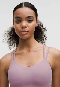 Reggiseno sportivo di colore viola chiaro con spalline sottili, caratterizzato da una texture liscia e un design minimalista. Nessun motivo visibile o dettagli in metallo.