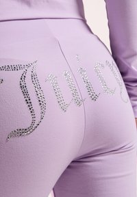 Lavendel Hosen aus weichem Stoff, ausgestattet mit silbernen Strassverzierungen, die auf der Rückseite "Juicy" buchstabieren und das Design unterstreichen.