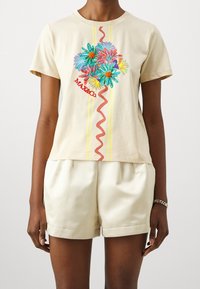 Camiseta de algodón de manga corta color crema, con bordado floral colorido y logo rojo, adornada con rayas verticales amarillas y un diseño de línea ondulada roja.