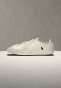 Λευκό casual sneaker με κορδόνια, χαμηλή σόλα και μικρό σκούρο λογότυπο παίκτη πόλο στο πλάι, εκτεθειμένο σε φωτεινή επιφάνεια.