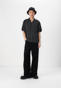 Cămașă cu dungi alb-negru, cu mâneci scurte și guler relaxat, asociată cu pantaloni negri cu picioare largi și încălțări chunky negre. Include și o pălărie.