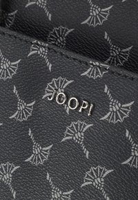 Materiale nero testurizzato con motivi grigi, con un logo che recita "JOOP!". Il design include dettagli intricati e una forma strutturata.
