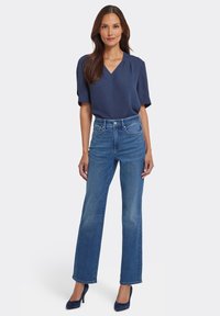 Mörkblå v-ringad blus med korta ärmar, kombinerad med ljusblåa högmidjade jeans med raka ben och mörkblå högklackade skor.