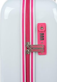Maleta rígida blanca con rayas rosas. Cuenta con dos cremalleras plateadas y un candado de combinación con base rosa y diales negros.