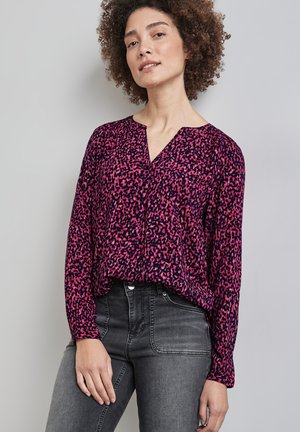 Roze en marineblauw gestreepte blouse met lange mouwen en een V-hals, voorzien van een losse pasvorm en een textuurstof. Gecombineerd met donkergrijze jeans.