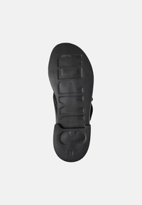 Black rubber shoe sole with embossed "CAMper" logo and size "38." Smooth texture, slightly curved shape, designed for comfort and grip.