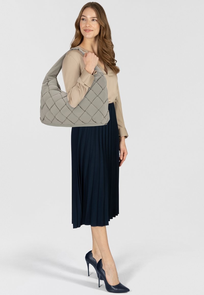 Szara pikowana torebka typu hobo noszona na ramieniu. Modelka ma na sobie beżową bluzkę i granatową plisowaną spódnicę oraz szpilki.