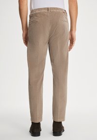 Brązowe spodnie sztruksowe o fakturowanym wykończeniu, z elastyczną talią i tylnymi kieszeniami. Noszone z czarnymi botkami przy kostce.