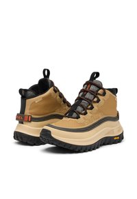 Bottes de randonnée imperméables couleur beige avec accents noirs, tige texturée, semelle épaisse et semelle extérieure multidirectionnelle. Caractéristiques un logo vibrant orange et des lacets assortis.