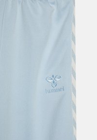 Lyseblåt stof med en hvid og blå chevronstribet kant og en synet hummel-logo nær højre kant.