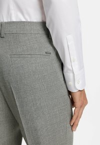 Szare spodnie o fakturze, zaprojektowane w fasonie slim fit z tylną kieszenią, połączone z białą koszulą z długim rękawem z guzikami.