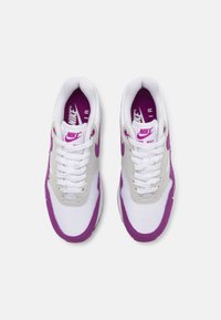 Par nogavic z belo in vijolično barvo Nike Air Max, z belimi vezalkami, vijoličnim Nike swoosh-om in vijoličnim notranjim znamčenjem, prikazane od zgoraj na belem ozadju.