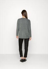 Szary sweter dziany z długimi rękawami, okrągłym dekoltem i luźnym krojem. Noszony z czarnymi podwiniętymi spodniami i czarnymi butami.