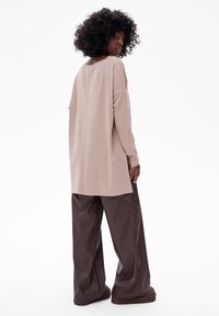 Beige langertrui met een relaxte pasvorm en ronde halslijn, gecombineerd met donkerbruine wijde broek van een gladde stof.