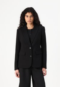 Blazer noir ajusté, à un bouton, avec revers crantés, deux poches avant et fermeture à trois boutons. Fabriqué à partir d'un tissu lisse au fini mat.
