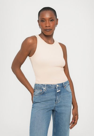 Beige ribbed tank top with a high neckline paired with light blue straight-leg jeans. The look features minimal hardware and a fitted silhouette.