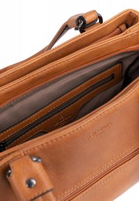 Interno di una borsa a tracolla in pelle tan con due scomparti con zip, una texture liscia e cuciture a contrasto. Presenta un'etichetta di marca e una tasca.