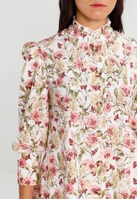 Robe à imprimé floral avec un col montant, des manches bouffantes et une patte de boutonnage à l'avant. Les couleurs dominantes sont le rose, le vert et le blanc, avec un tissu texturé.