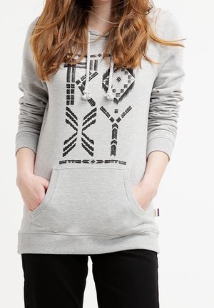 Grå huvtröja i mjukt tyg med en kenguruficka. Har svart geometriskt mönster och huva med dragsko. Ribbstickade muddar.