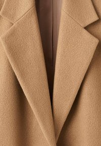 Cappotto in lana color tan con rever a scialle, tessuto testurizzato e foderato in marrone liscio, che mette in evidenza un design sartoriale e strutturato.
