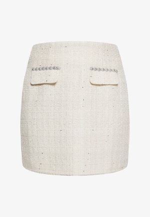 Mini-jupe en tweed blanc avec deux poches avant ornées d'accents argentés décoratifs et un tissu texturé avec de petits fils brillants.