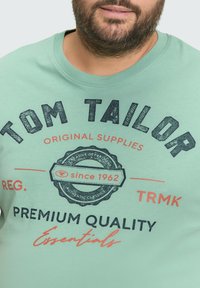 Lichtgroene katoenen t-shirt met een ronde halslijn en een grafische print aan de voorkant. De tekst bevat "TOM TAILOR" en details in marineblauw en koraalkleur.
