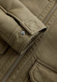 Olivgrüne Lederjacke mit strukturiertem Finish, ausgestattet mit einem Reißverschluss und einem Druckknopfdetail an den Ärmelbündchen.