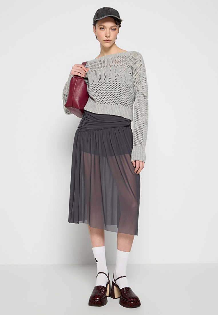 Grauer Strickpulli im Oversized-Schnitt, grauer plissierter Midirock, burgunderfarbene Handtasche, weiße Socken und glänzende braune Pumps.