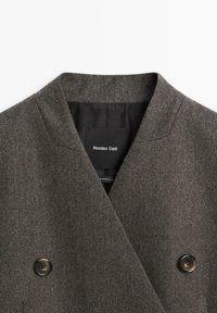 Brązowy dwurzędowy płaszcz z mieszanki wełny z klapami, dwiema guzikami oraz metką "Massimo Dutti" wewnątrz. Teksturowana powierzchnia materiału.