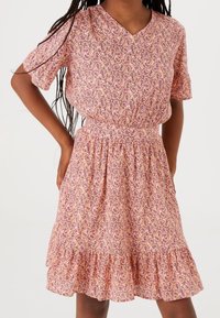 Květinové šaty v růžové barvě s fialovými akcenty, s výstřihem do V, krátkými rukávy, elastickým pasem a volánkovým lemem. Lehce se nosí.