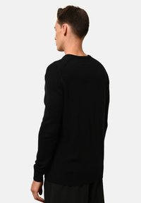 Svart, stickad tröja med rund halsringning, raglanärmar och ribbad nederkant och ärmar. Tyget ser mjukt och strukturerat ut. Utsikt bakifrån.