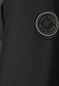 Sort tekstureret stof med et rundt sort og hvidt CMS Sport logo patch syet på det øverste højre område.