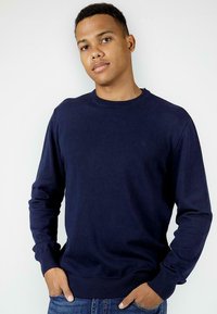 Granatowy sweter z okrągłym dekoltem, wykonany z miękkiego materiału, z długimi rękawami oraz ściągaczami na mankietach i dole. Prosty design bez widocznych wzorów.