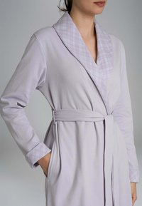 Accappatoio di un leggero lavanda con colletto a scialle caratterizzato da un motivo a quadri. Ha una vita con cintura e tasche laterali, realizzato in tessuto morbido.