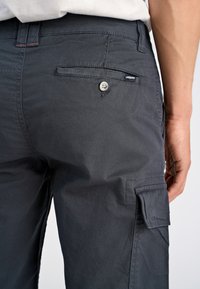 Pantaloni cargo grigio scuro in tessuto testurizzato, con tasche posteriori con bottone e una tasca cargo laterale. Presentano dettagli di cucitura discreti e un'etichetta del marchio.