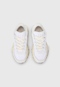 Zapatillas blancas con una mezcla de materiales lisos y texturizados. Presentan acentos en amarillo, detalles en beige y cordones de color claro.