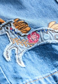Il tessuto in denim ricamato presenta un design colorato di un cavallo con criniera marrone, fiore rosa e accenti blu su uno sfondo azzurro chiaro.