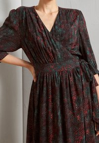 Robe portefeuille en tissu à imprimé serpent de couleur bordeaux foncé et sarcelle. Dotée d'un décolleté en V, de manches courtes bouffantes et d'une taille nouée pour une coupe ajustée.