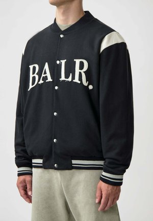 Black varsity jacket with "BALR." embroidered in cream. Features cream-colored shoulder accents and striped ribbed cuffs and hem.