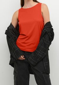 Rød ribbet tanktop parret med en oversized sort jakke med et hvidt gittermønster og sorte cargo-bukser.
