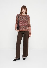 Strikkegenser i varme toner med et teksturert mønster, parret med brune vidde bukser og svarte ballerinasko. Liten svart crossbody-veske inkludert.