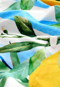 Baumwollstoff mit einem botanischen Druck, der grüne Blätter, gelbe Zitronen und blaue Akzente zeigt, mit lebendigen Aquarelltexturen.